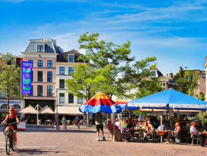 A man rides his bike down a street, flanked by tall buildings, capturing the blend of urban life and cycling culture, Utrecht, Netherlands