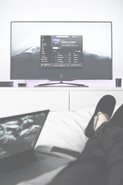 A man using a black remote control on crisp white bed sheets