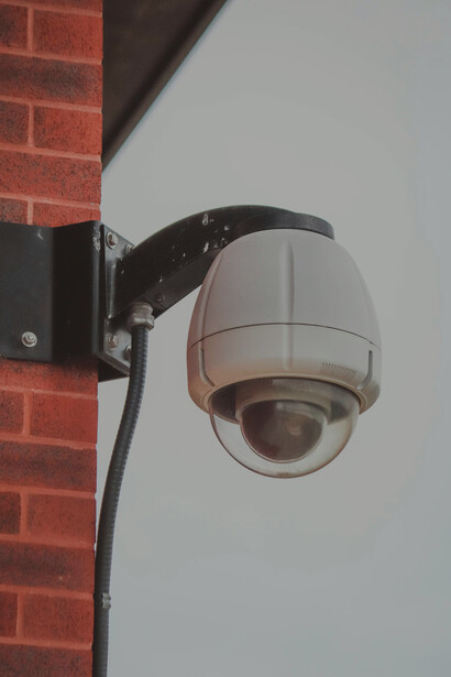The security camera attached to the brick building symbolizes the growing presence of surveillance technology and its implications for data privacy