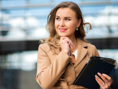 A professional woman engaging with her digital tablet outside a contemporary office building, illustrating women's economic empowerment