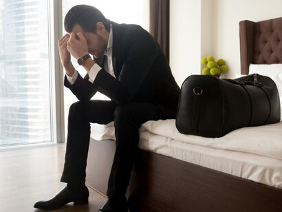 A stressed man sits on his bed, holding his head, struggling to overcome his difficulties
