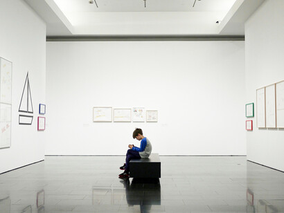 Assorted paintings on a white wall, illuminated by museum-standard lighting, showcasing gallery light design for art conservation
