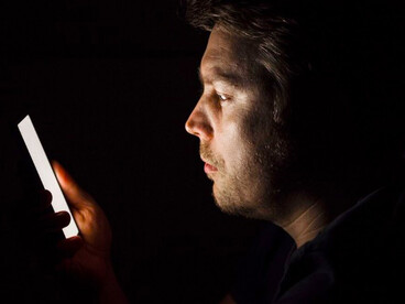 In the silence of night, a man looks down at his phone, illustrating the growing tension between loneliness and technology