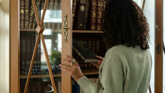 Parada en camisón, junto a la biblioteca, Josefina selecciona al azar un tomo negro