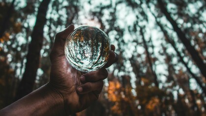 Mão segura uma esfera de vidro que reflete a floresta ao redor. A sustentabilidade tornou-se um dos principais indicadores de credibilidade e valor nos mercados de capitais contemporâneos. O equilíbrio entre crescimento econômico, transparência e responsabilidade ambiental está no centro das discussões sobre ESG. O futuro do investimento global passa cada vez mais pela integração de critérios sustentáveis e práticas de governança. Em mercados emergentes como Moçambique, sustentabilidade e confiança institucional caminham lado a lado. A pressão internacional por relatórios ambientais e sociais redefine a relação entre empresas e investidores