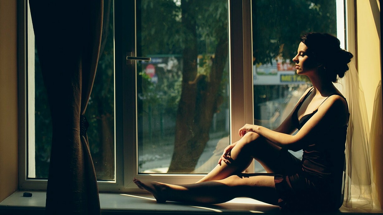 A woman sitting quietly by a sunlit window, representing the emotional patterns carried from childhood into adulthood