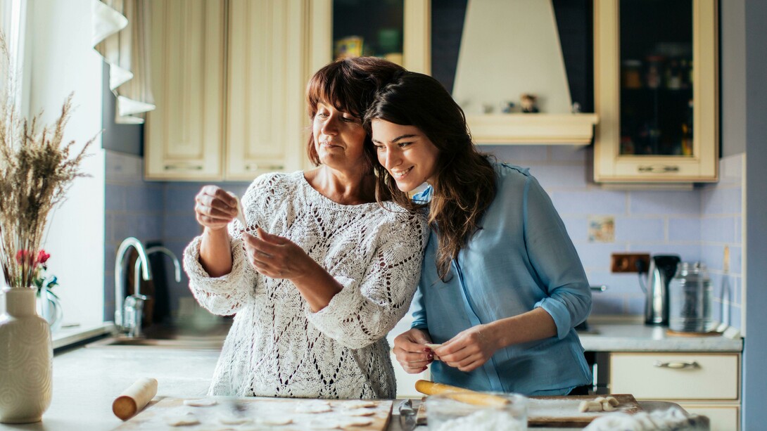 A woman in a blue long-sleeve shirt cooking in the kitchen with her mother
