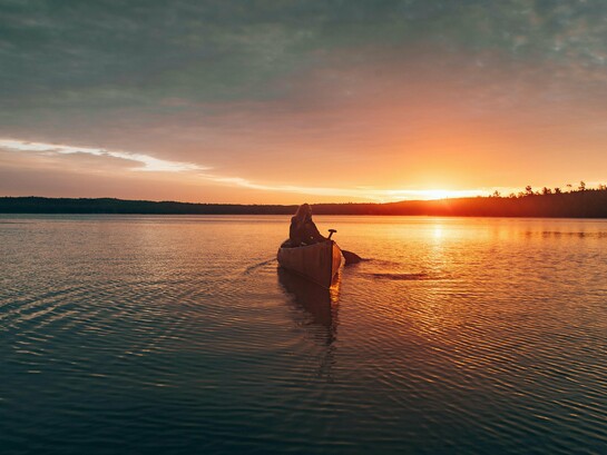 A woman drifting through Ely Lake, Minnesota beneath the fading Minnesota sky, reflecting the deep connection between nature, solitude, and healing