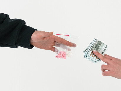 A juxtaposition: one hand extending money, the other presenting illicit drugs