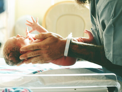 A person in a gray shirt is placing a newborn baby on a scale for measurement