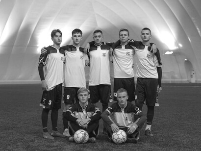 Young footballers standing together on a green pitch, surrounded by the facilities of a state-of-the-art training academy