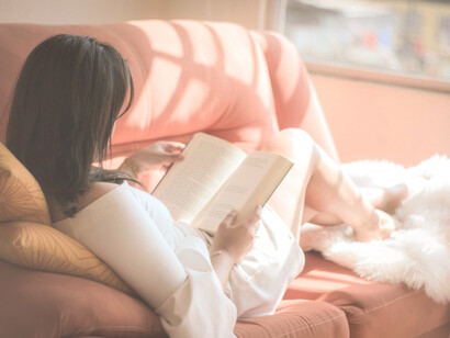 Mujer acostada en el sofá, lee un libro con la luz de la tarde