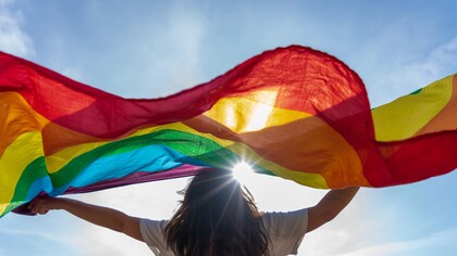  A young woman waving LGBTQIA+ flag under the sky