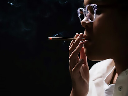 In a close-up frame, a woman with white sleeves and chic eyeglasses embraces a captivating smoking scene