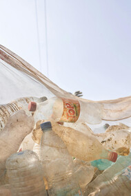 A low-angle photograph captures people carrying a garbage bag full of plastic bottles