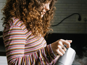 A woman prepares coffee in a quiet kitchen with soft, natural lighting