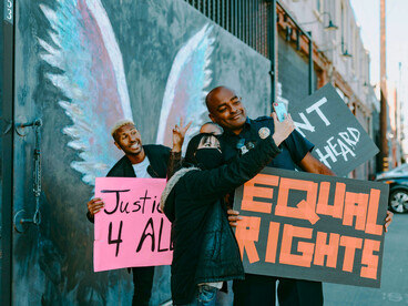 A group holding placards with social messages and snapping photos, reflecting how protests extend beyond physical spaces