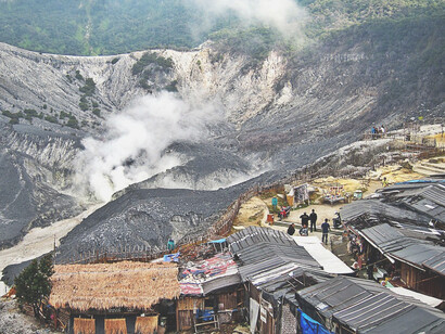 The craters of Tangkuban Perahu in Bandung, Indonesia, loom mysteriously in the morning mist, with thick white smoke billowing from the still-active volcanic vents, creating a surreal and enchanting atmosphere