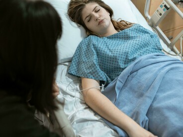 A woman gently holding a patient’s hand in a hospital, expressing warmth and compassion