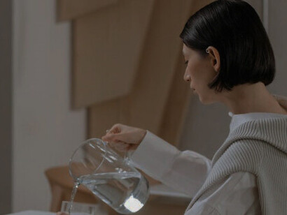 The woman carefully pours water from a jug into a glass