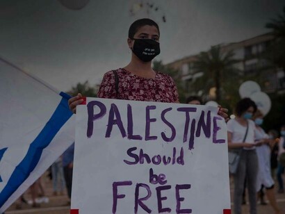 An Israeli waving a flag while carrying a sign reading "Palestine should be free"