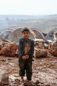 A young boy stands in the mud at a refugee campsite