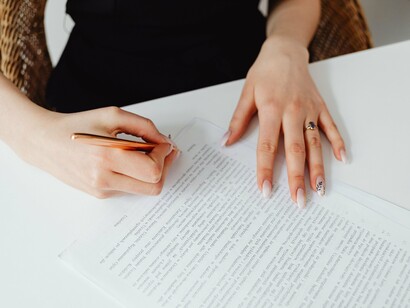 As mãos de uma mulher escrevem em um documento, concentrando no papel uma tarefa aparentemente simples e cotidiana. No texto, porém, o preenchimento de um campo revela uma ausência que atravessa toda uma história: a responsabilidade paterna que nunca chegou a se materializar