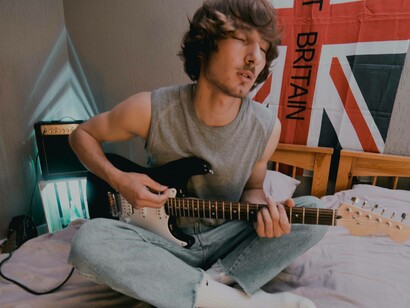 A young man closing his eyes to concentrate and help the creativity flow on his guitar