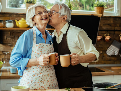 An elderly husband and wife laughing and dancing in their kitchen