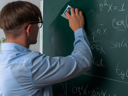 A young male mathematician wearing glasses stands by a blackboard, writing equations with confidence