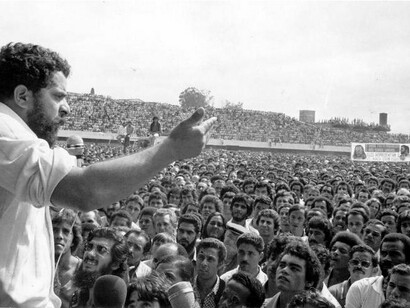 Luiz Inácio Lula da Silva discursa diante de uma multidão de trabalhadores, em uma imagem que registra a força da mobilização operária em torno de sua liderança. Décadas depois, aquele dirigente sindical chegaria à Presidência da República, levando para a política institucional uma trajetória construída no movimento dos trabalhadores