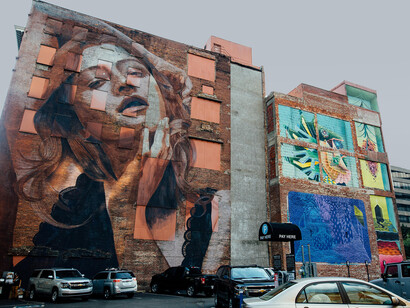 Graffiti spreads across a worn city building, set against a moody, cloud-filled sky