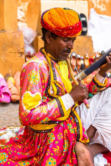 Seated on the ground, a man plays a musical instrument with quiet focus, India