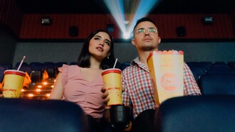 A couple at the cinema have their popcorn and drinks and are eagerly anticipating the movie they are about to watch