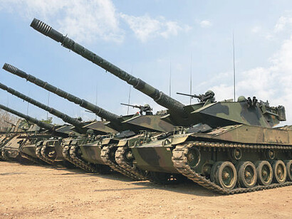 A lineup of heavy military tanks with large cannons positioned on a training ground for inspection and operational readiness