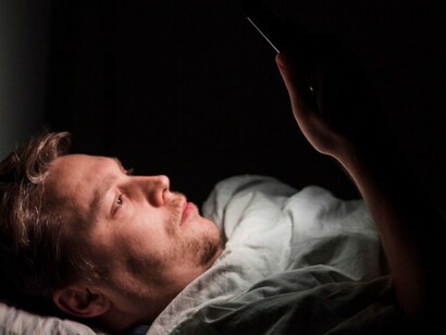 A man sits late at night, staring at his phone, reflecting the quiet intersection of depression and digital technology