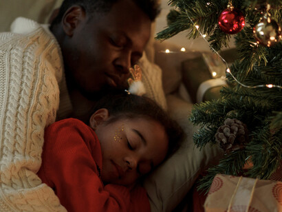 Pai e filha adorcem juntos ao lado de árvore de Natal e presentes