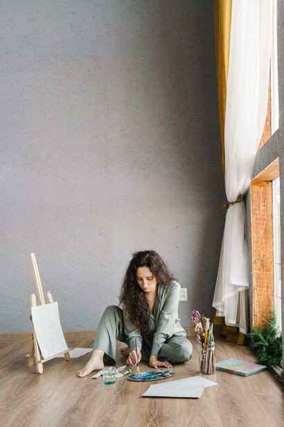 A young woman on the floor busy painting, taking on a hobby, will help your mental well being