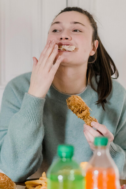 A woman eating fried chicken and a burger at a table, representing the temptation of ultra-processed fast food