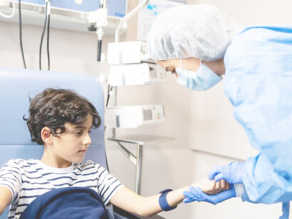 Boy in chemotherapy looking at a nurse finding a vein on his arm