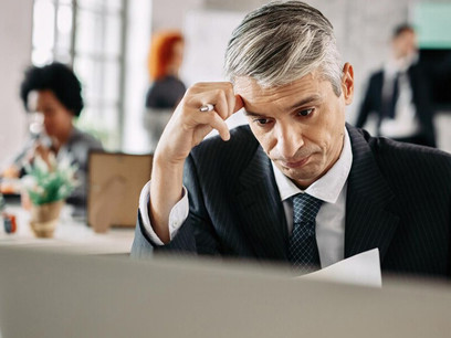 An overworked businessman rests his head on the desk, exhausted, while colleagues in the background display signs of stress, anxiety, and conflict—capturing the essence of a toxic workplace filled with unhappy, burned-out employees