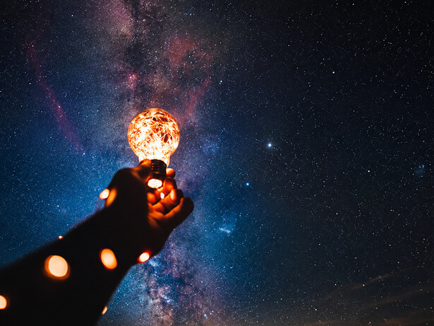 Uma mão ergue uma lâmpada acesa diante de um céu estrelado, em uma metáfora para o surgimento de novas ideias e descobertas. A inovação científica nasce da curiosidade, mas só transforma a sociedade quando o conhecimento é desenvolvido, protegido e colocado em prática. A mão segurando uma lâmpada acesa diante de um céu estrelado remete à criatividade, ao conhecimento e ao potencial transformador da ciência. Em vez de representar o ambiente laboratorial, ela sintetiza visualmente a ideia de que uma descoberta pode iluminar novos caminhos quando é convertida em inovação