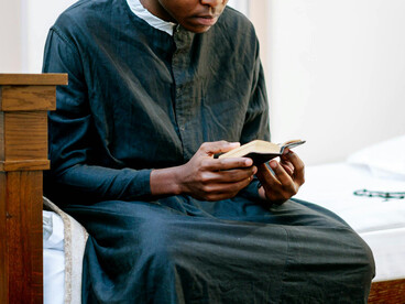 A man in black attire holding a Bible as he prays in silence