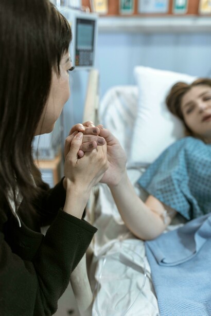 Hospital visitor clasping a patient’s hand in a caring and emotionally supportive gesture