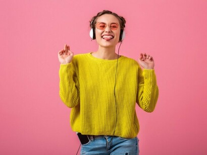 A woman dressed in a colorful hipster style listens to music through headphones, enjoying a viral track