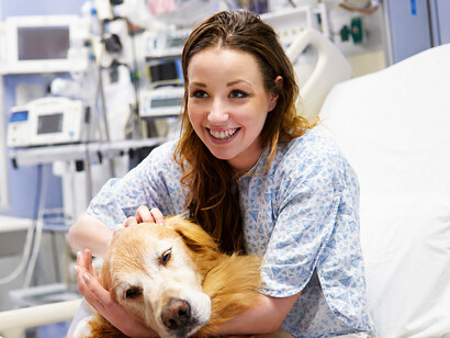 A young female patient receives a comforting visit from a therapy dog inside a hospital room