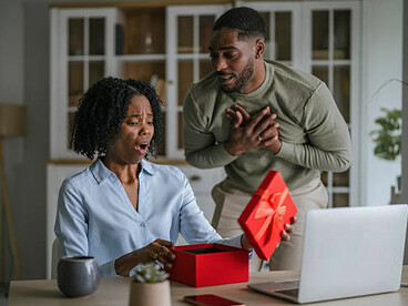 Woman appearing uncomfortable as she receives a gift from her partner, suggesting emotional pressure behind the gesture