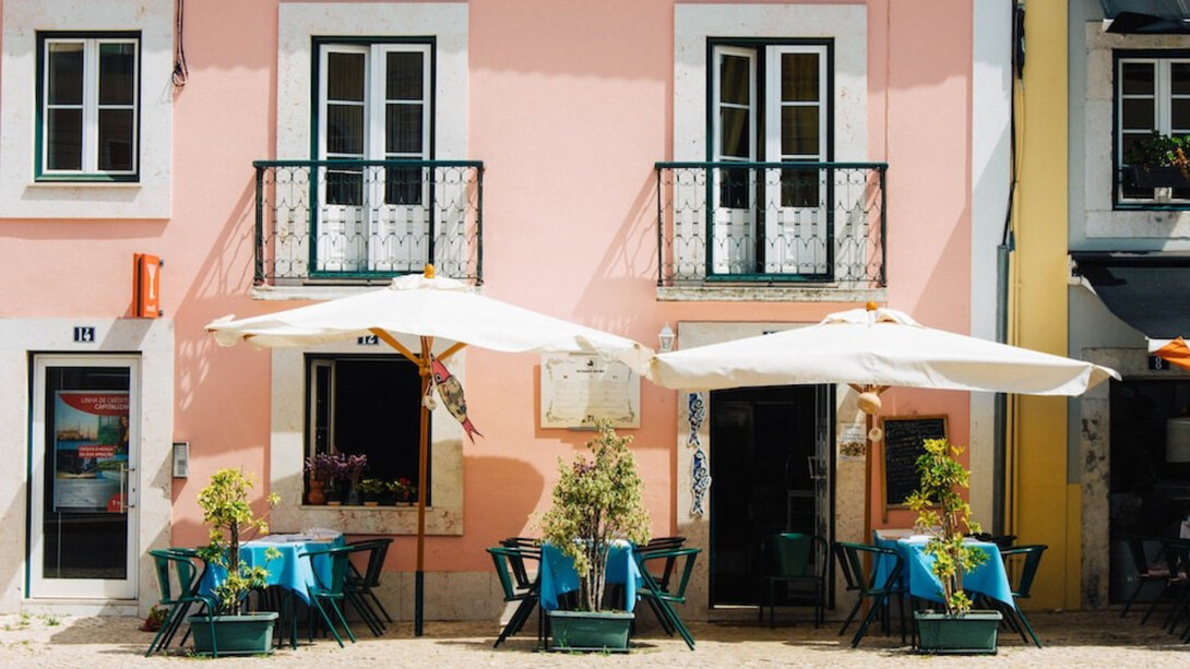 Adoring Lisbon's charms, two white patio umbrellas grace a pink and white painted building, Portugal