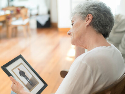 Back view of an elderly woman holding a framed photograph while grieving