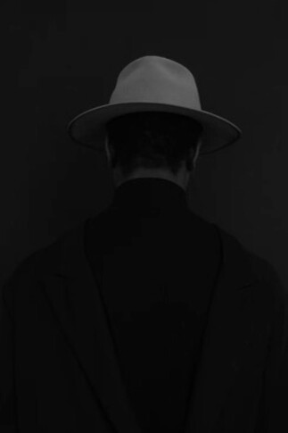 A mysterious man in a black suit and white fedora, reminiscent of a 1940s gangster